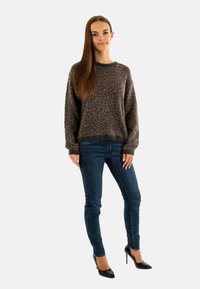 Pull à imprimé léopard en tissu doux, dans des tons marron et noir. Associé à un jean skinny bleu et des escarpins noirs à bout pointu.