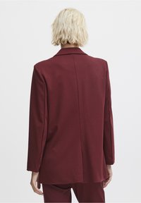 Blazer bordeaux avec une coupe ajustée, fermeture à un bouton, revers crantés, et manches longues. Texture douce avec une finition lisse.