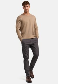 Pull beige à col en V associé à un pantalon noir gris bien ajusté, avec une texture lisse et une coupe fitted. Des chaussures marron viennent compléter le look.