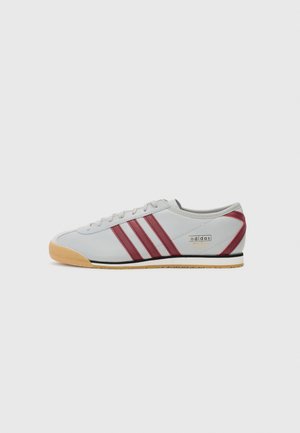 Zapatilla atlética gris con tres franjas color burdeos, cordones blancos y suela de goma. Presenta un diseño elegante y detalle del logo "adidas Italia".