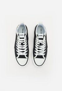Sorte lerretsneakers med hvite gummitupper og såler, med hvite snørebånd og merkevare på tungen. Utformet for uformell bruk.