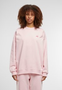 Rosa oversized sweatshirt med rund hals og ribbestrikkede mansjetter. Har en liten logo på brystet. Myk tekstur, avslappet passform.