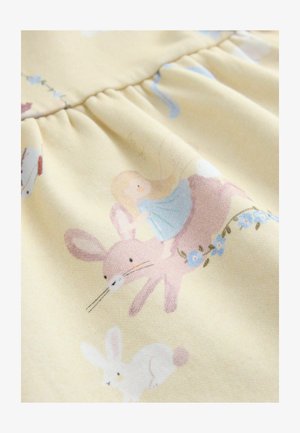 Lysegult stof med et mønster af kaniner og en pige i en blå kjole med blomsterdetaljer. Teksturen er blød og let draperet.