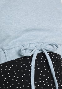 Světle modrý top s texturovaným povrchem a stahovacími šňůrkami v pase, kombinovaný s černou tkaninou s bílými puntíky.