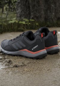 Black hiking shoes with gray accents, featuring a mesh upper, rugged sole, and red detailing on the heel and laces. Terrex branding visible.