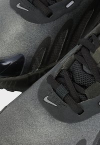 Baskets Nike noires avec une finition mate, un tissu texturé et des lacets noirs. Présente un accent en caoutchouc brillant et des détails de marque minimalistes.