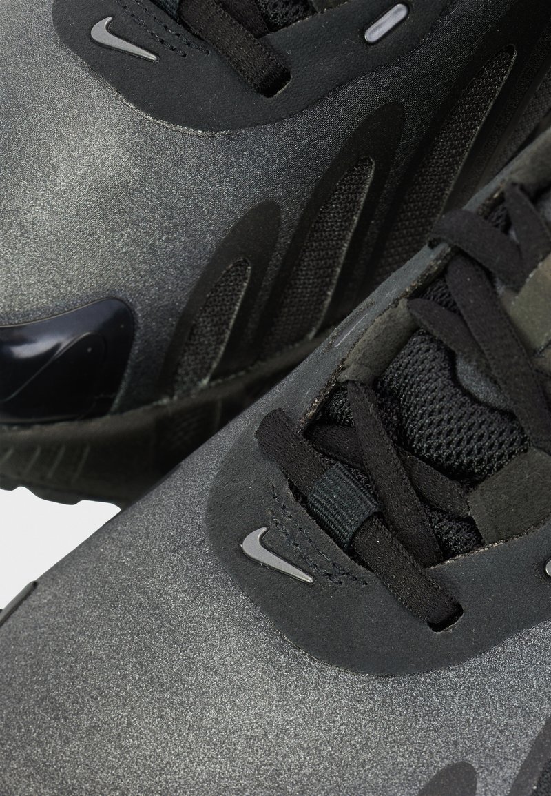 Zapatillas Nike negras con acabado mate, tejido texturizado y cordones negros. Presentan un acento de goma brillante y detalles de marca mínimos.