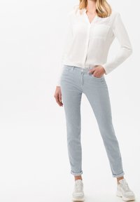 Bílá košile s dlouhými rukávy a přední kapsou, spárovaná s světle modrými pruhovanými slim-fit džíny, nošena s bílými teniskami. Jednoduchý a čistý design.