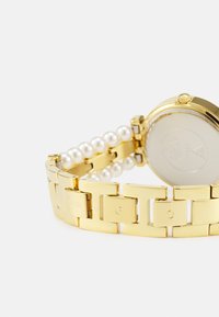 Gold watch with a metal band featuring glossy links, accented by a row of pearl-like beads; round case with a polished finish.