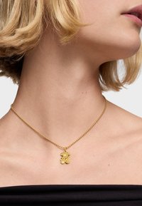 Złoty naszyjnik z łańcuszkiem w formie kulki i kwiatowym wisiorkiem. Wisiorek charakteryzuje się misternym zdobnictwem i teksturowaną powierzchnią w kontakcie z nagą skórą.