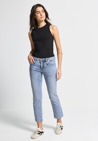 Bodysuit negro sin mangas combinado con jeans azul claro. Los jeans tienen un corte relajado, un ligero desgaste y un diseño de cinco bolsillos. Las zapatillas son beige con acentos negros.