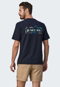 Tamsiai mėlynas medvilnės marškinėliai su daugiakampiu kalnų logotipu ir „patagonia“ tekstu ant nugaros. Trumpomis rankovėmis ir laisvu siluetu.