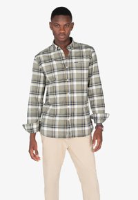 Camisa verde a cuadros con mangas largas y cierre frontal de botones. Presenta líneas blancas y marino; se lleva con pantalones beige.