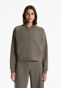 Leicht olivgrüner Reißverschluss-Hoodie aus strukturiertem, geripptem Stoff. Mit Kapuze und Raglanärmeln; crop-cut mit enganliegenden Bündchen.