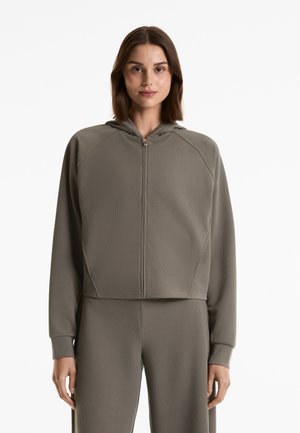 Felpa con zip di un verde oliva chiaro, realizzata in un tessuto ribbed testurizzato. Presenta un cappuccio e maniche raglan; lunghezza cropped con polsini aderenti.