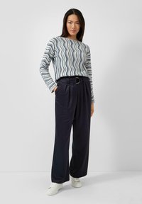 Gestreept shirt met lange mouwen met golvend patroon in blauw, wit en grijs, gecombineerd met marineblauwe wijde broek met hoge taille en witte sneakers.