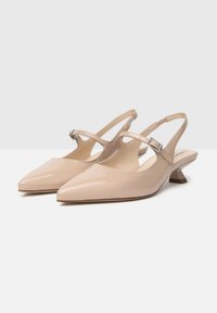 Chaussures à talon ouvert beige à bout pointu avec une finition laquée brillante, présentant un design à découpes, une fine bride et un petit talon carré.