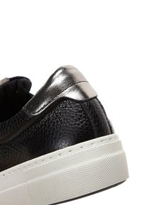 Zwarte leren sneaker met een gestructureerde afwerking, metallic zilveren accent bij de hiel en een witte rubberen zool met een patroon.