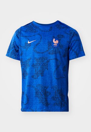 Blue athletic shirt made of smooth fabric features a dark abstract pattern, a small orange Nike logo, and a crest with a rooster emblem.