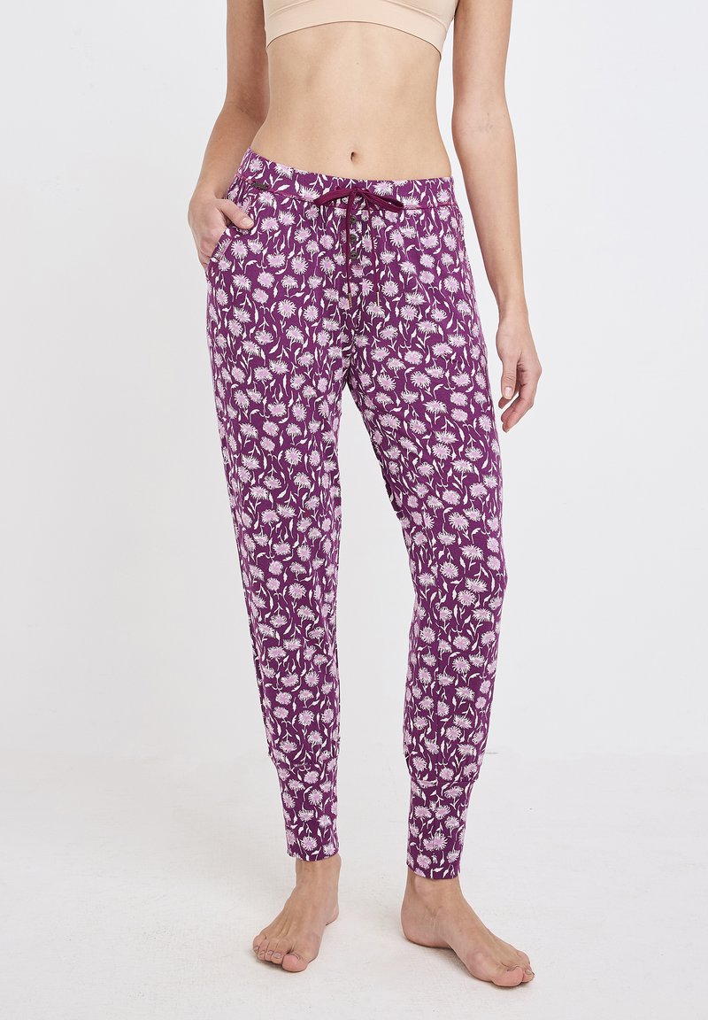 Fioletowe spodnie piżamowe z białym wzorem kwiatowym, wykonane z miękkiego materiału. Posiadają elastyczny pas i boczne kieszenie. Dopasowane mankiety przy kostkach.