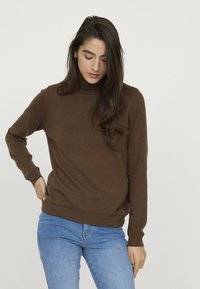 Pull en tricot marron avec un col montant, des manches longues et des poignets côtelés. Assorti à un jean en denim bleu. Texture lisse.