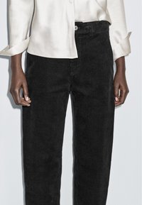 Zwarte corduroy broek met verticale ribbels, ontworpen met een hoge taille, voorzien van een sluiting met een knoop aan de voorkant en zijzakken.