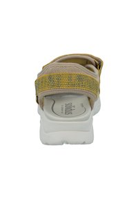 Beige sandal with woven yellow and blue accents, flexible upper, cushioned insole, and white outsole with textured grip patterns.