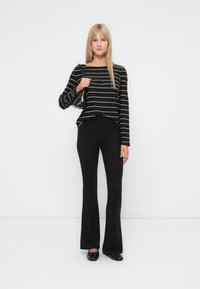 Svart og beige stripet langermet topp med rund hals, parret med svarte ribbede flare-bukser og svarte flate sko. Liten håndveske.