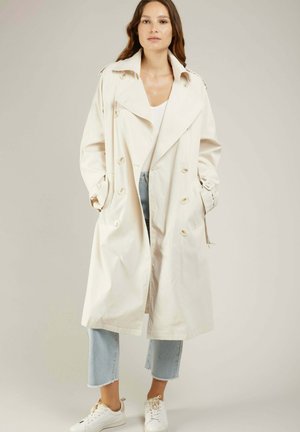 Manteau beige avec un design à double boutonnage, grand col et détails de boutons. Manches longues avec poignets ceinturés. Tissu léger.