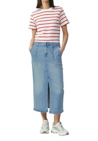Witte T-shirt met rode horizontale strepen, gecombineerd met een lichtblauwe denimrok met een split aan de voorkant en twee zijzakken. Gekozen voor witte sneakers.