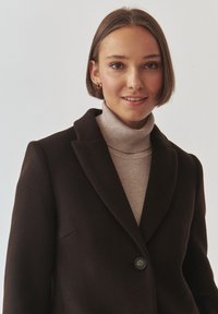 Bruine wolmix blazer met een notch lapel en één knoopsluiting, gedragen over een lichtbeige turtleneck met een gladde textuur.