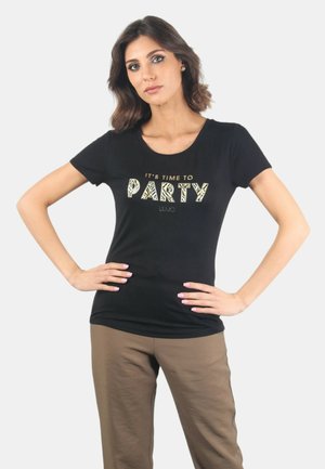 T-shirt nera con scollatura a barca e maniche corte, caratterizzata da una grafica dorata e a fantasia con la scritta "PARTY". Abbinata a pantaloni beige.