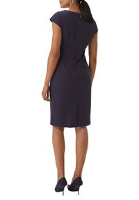 Marineblaues, tailliertes Kleid mit kurzen Ärmeln, Reißverschluss hinten und strukturierten Nähten. Kombiniert mit passendem, hohen Schuhen, die eine glatte Beintextur zur Geltung bringen.