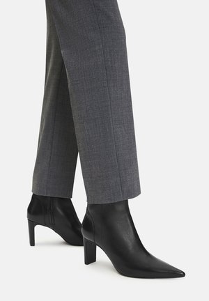 Czarne skórzane botki za kostkę z szpiczastym noskiem i szerokim obcasem, zestawione z szarymi, dopasowanymi spodniami o subtelnej fakturze i kantem.