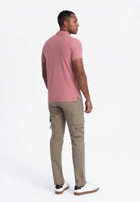 Vaaleanpunainen polo-paita, khaki-väriset cargo-housut, joissa on sivutaskut, ja valkoiset lenkkarit mustilla yksityiskohdilla. Pehmeät tekstuurit, rento istuvuus.