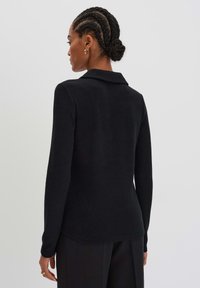 Schwarzer Strickpullover mit Kragen, langen Ärmeln und abgerundetem Saum, mit einer glatten Textur. Die Rückansicht zeigt eine figurnahe Silhouette.