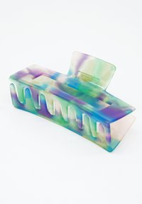 Flerfärgad hårklämma gjord av genomskinlig plast, med en vågig design, slät yta och en rektangulär öppning för säker grepp.
