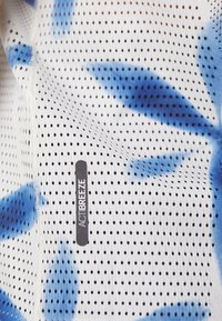 White mesh fabric with dark blue leaf patterns, featuring small perforations. Includes a black label with "ACTIBREEZE" printed on it.