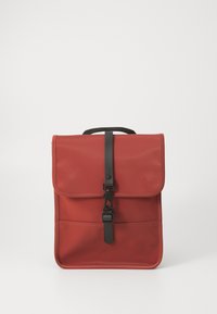 Red backpack made of durable synthetic material, featuring a front flap with a black buckle closure and a top carry handle.