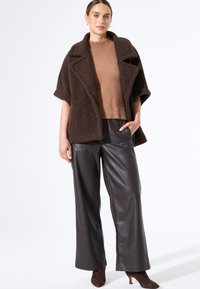 Bruine gestructureerde blazer met grote revers, gedragen over een lichtbruine gebreide top. Gecombineerd met donkerbruine leren broek met hoge taille en wijde pijpen.