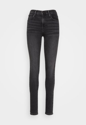 Skinny jeans in black denim, featuring a high waist, five pockets, and subtle whiskering on the front for texture and style.