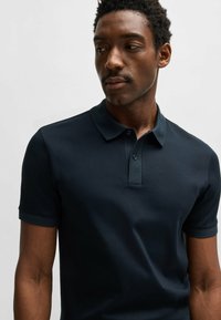 Mörkblå polotröja i slät bomull med knappslå, korta ärmar och subtil krage; den figurnära designen sitter tight mot kroppen.