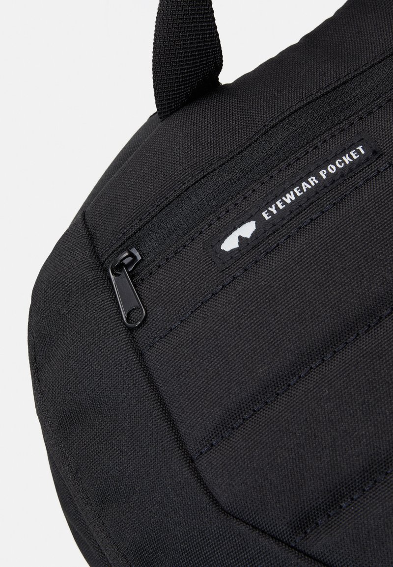Custodia per occhiali in tessuto nero con chiusura a zip e superficie testurizzata. L'etichetta riporta la dicitura "CUSTODIA PER OCCHIALI" con un'illustrazione di occhiali.