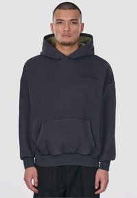 Kulsort pullover hoodie med en frontlomme, ribbede manchetter og kant; har et tonet logo på brystet og en olivenfarvet inderside.