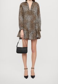 Kjole med leopardprint og et trinvist design, lange ærmer og V-udskæring. Sort håndtaske med skulderrem, kombineret med spidse hæle.