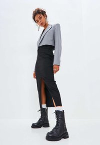 Blazer gris corto, falda negra con abertura y botas de tobillo negras con cordones y suelas texturizadas; joyería de plata realza el conjunto.