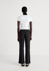 White short-sleeve t-shirt paired with high-waisted, dark gray pinstriped trousers. Trousers feature two back pockets and a flared leg design.