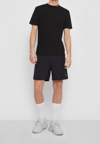 Svart bomullströja med hög halsringning, kombinerad med svarta träningsshorts och vita ankelsockor. Vita sneakers med grå detaljer.