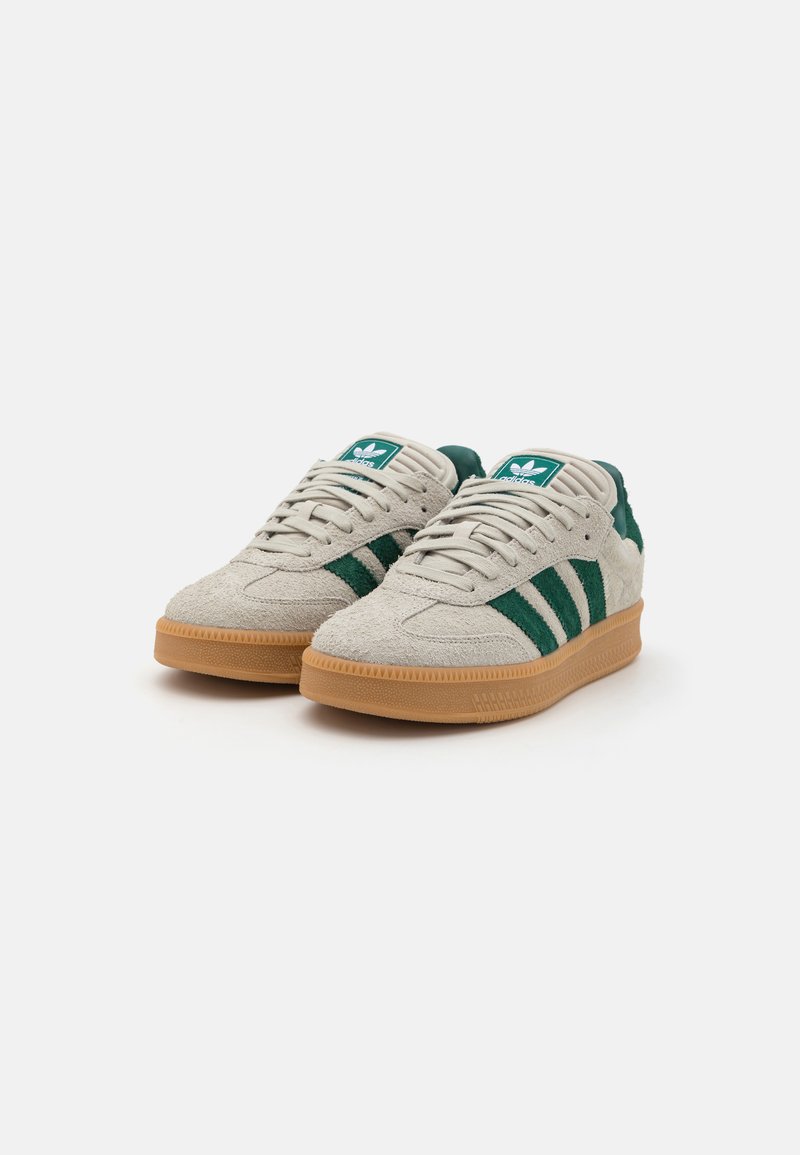 Zapatillas de ante en color crema con rayas verdes, con una parte superior texturizada, lengüeta acolchada y suela de goma.