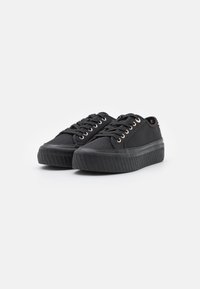 Para czarnych niskich sneakersów z teksturowanymi podeszwami i czarnymi sznurówkami, umieszczona na czystej białej powierzchni, skierowana w przód.